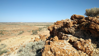 A rocky outcrop overlooks a vast, orange plain dotted with shrubs at Evelyn Downs.
