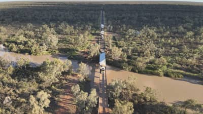 Aerial view of truck carrying a portable house through the countryside and crossing a river.