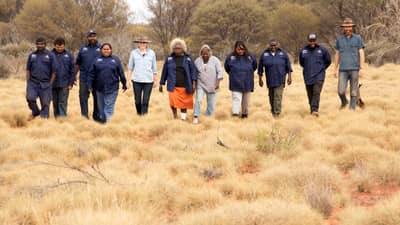 A group of 9 Birriliburu rangers with Vanessa Westcott & Hamish Morgan spread out and walking towards camera.