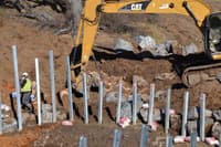 Major earthworks setting steel beams to hold back a rock wall.