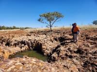 Two Aboriginal men look at a waterhole surrounded by mottled rust red, orange and white rock at Edgbaston Reserve.
