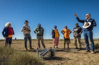 Ecologist Nick Leseberg stands on Pullen Pullen Reserve, speaking to a group of Indigenous rangers in front of a motion-sensor camera installation.