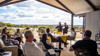 Two people are presenting in an under cover outdoor area at the Red Moort Field Station to an audience of gathered onlookers.