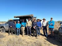 A large group of nine Bush Heritage and Pastoral Partners staff pose for a group photo in front of their vehicles.