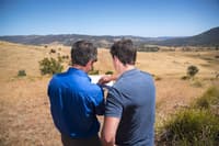 Ecologist Matt Appleby looks at a document with a farmer. Both are facing away from the camera and looking towards farmland.
