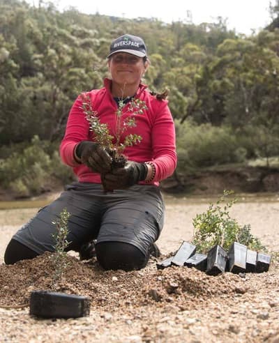 UMDR Facilitator Antia Braderman planting seedlings by the river.