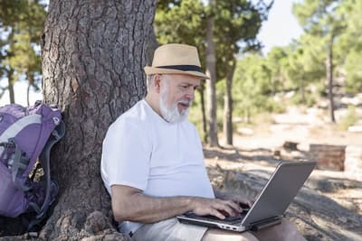 Man sitting under a tree and using a laptop computer.