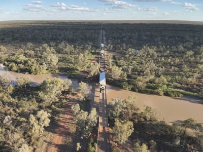 Aerial view of truck carrying a portable house through the countryside and crossing a river.
