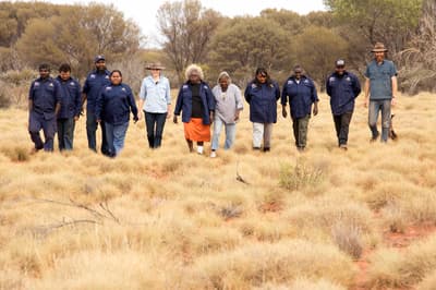 A group of 9 Birriliburu rangers with Vanessa Westcott & Hamish Morgan spread out and walking towards camera.