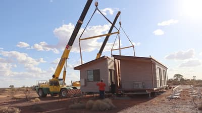 Mobile cranes lifting two halves of a portable building into place.