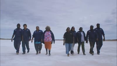 Group of nine Birriliburu rangers walk towards camera across a salt lake.