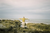 Bush Heritage Data Intern Nick Outram stands on a rocky seashore with his arms outstretched.