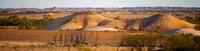 Two low hills rise out of a dry, orange plain broken up by scattered patches of gum-tree forest at Evelyn Downs.