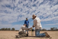 Three Bush Heritage staff setting up a motion sensor camera beside a track at Naree Station Reserve.