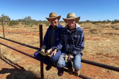 Bush Heritage volunteers Jack and Marja, an older couple, perch on a wooden fence together at Pilungah Reserve, smiling at the camera.