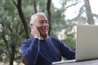 Senior man using his laptop while speaking on his mobile phone.
