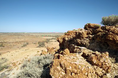 A rocky outcrop overlooks a vast, orange plain dotted with shrubs at Evelyn Downs.