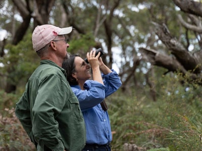 Peter Turnbull and Susan Ball looking through binoculars at their bushland property.